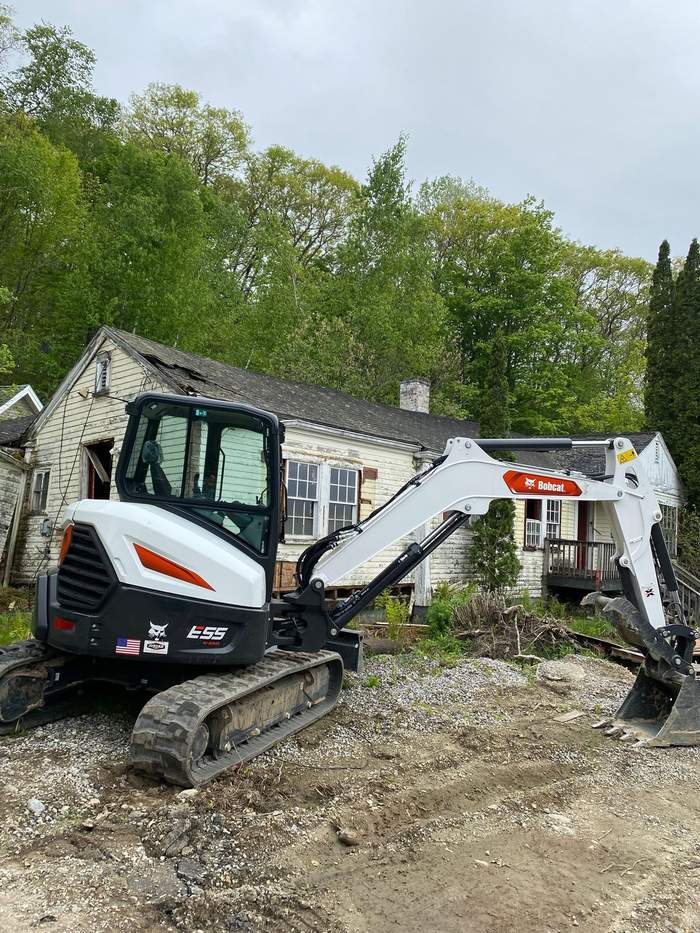 House before demolition, excavator staged on site
